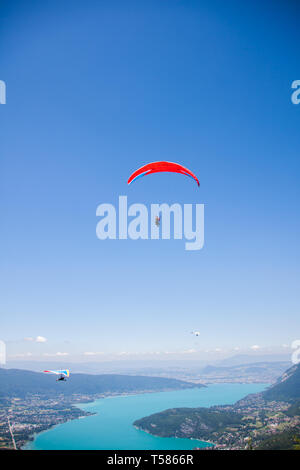 Drachenflieger und Paraglider Fliegen über See von Annecy durch Berge und Städte Stockfoto