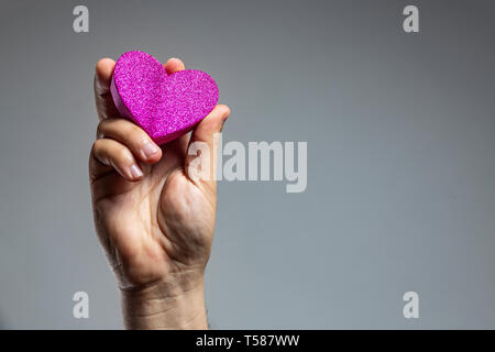 Nahaufnahme einer Hand, die eine rosa Herzform Stockfoto