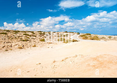 Eine gelbe Auto auf einer kurvenreichen Asphaltstraße von rauhen an Kalkstein Küste in der Nähe von Kap Greco, Zypern. Viele weiße Wolken am Himmel, kargen orange Sandy hi Stockfoto