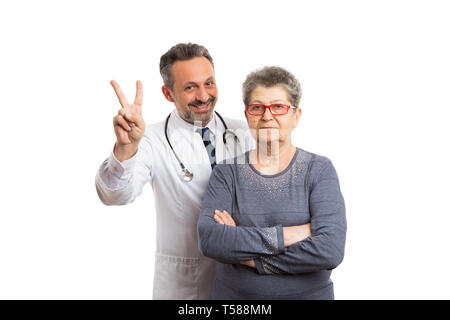 Scherzen männlicher Arzt, Frieden oder Sieg mit Seröser älteren weiblichen Patienten auf weißem studio Hintergrund isoliert Stockfoto