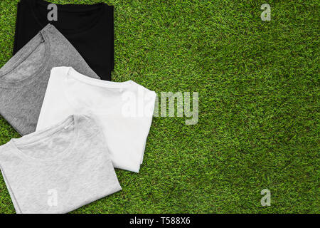 Stapel angeordnet verschiedene farbige mens T-Shirt auf Gras Hintergrund. Horizontale Ansicht. Stockfoto