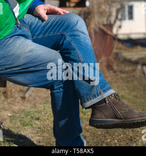 Ein Mann in Jeans und Jacke Sitzen im Freien, close-up Side Shot Stockfoto