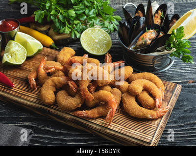 Gebratene panierte Garnelen, Muscheln serviert mit Kalk auf Holzbrett, köstlichen tiefen, roten, weißen Sauce Stockfoto