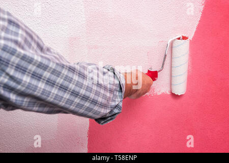 Kaukasische Haus Maler Arbeiter, malen die rosa Wand mit weißen mit dem Roller lackieren. Bauindustrie. Arbeitssicherheit. Stockfoto