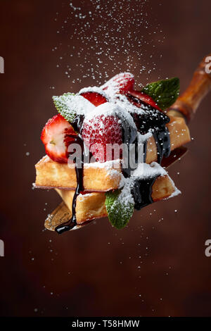 Waffeln mit Erdbeeren, Minze und Schokoladensauce, bestreut mit Puderzucker. Stockfoto