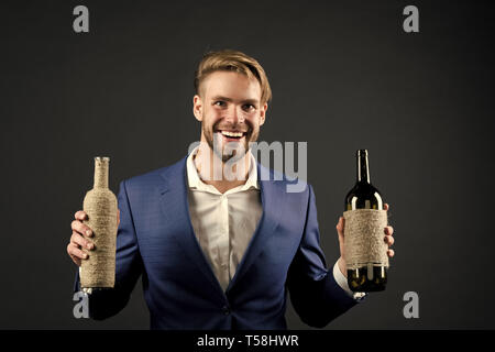 Sommelier halten zwei Flaschen Wein. Professionelle Weindegustation Konzept. Mann Anzug mit Wein Flaschen in den Händen. Sommelier schöne fröhliche Kerl auf dunklem Hintergrund. Welcher Wein gefällt Ihnen. Stockfoto