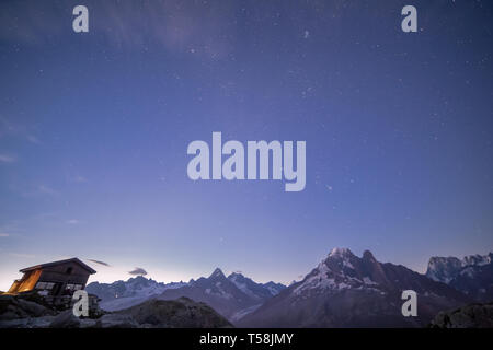 Berghütte in der Dämmerung mit schneebedeckten Gipfeln unter blauem Sternenhimmel Stockfoto