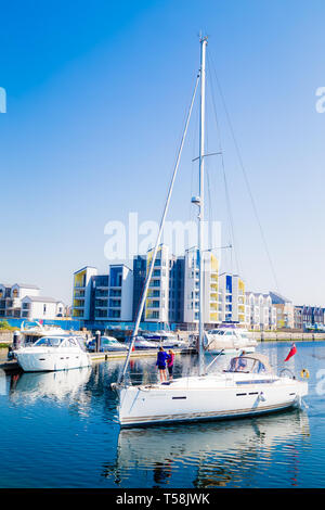 Eine Yacht mit einem hohen Mast vorbei Luxury Apartments in St Mary's Island im Chatham Maritime Marina. Kent. Großbritannien Stockfoto