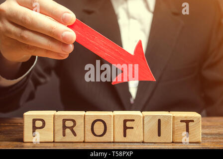 Ein Geschäftsmann ist mit einem roten Pfeil nach unten über die holzklötze mit dem Wort profitieren. Erfolglose unternehmen. Verlust von Investitionen. Geringen Gewinn. Kleine Einkommen Stockfoto