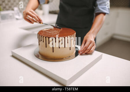Konditor bereitet einen Kuchen in der Küche. Weibliche Konditor Verbreitung Schokolade Zuckerguss über einen Kuchen. Stockfoto