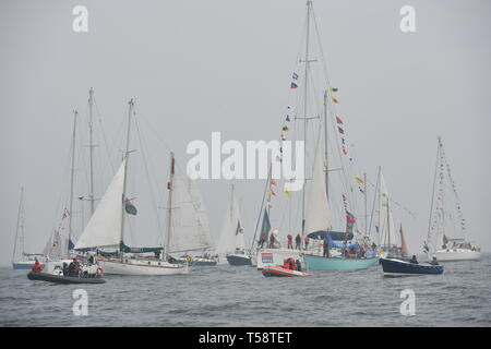 Sir Robin Knox-Johnson an Bord Suhali, wird durch eine Flotte von Schiffen über die Ziellinie seiner ursprünglichen Reise in Falmouth begleitet, zum 50. Jahrestag seiner Fertigstellung des ersten solo Non-stop-Weltumrundung. Stockfoto