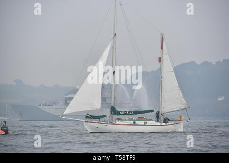 Sir Robin Knox-Johnson an Bord Suhali, vorbei an einem Kriegsschiff der Royal Navy, als er die Ziellinie von seinen ursprünglichen Reise in Falmouth zu überqueren, zum 50. Jahrestag seiner Fertigstellung des ersten solo Non-stop-Weltumrundung. Stockfoto