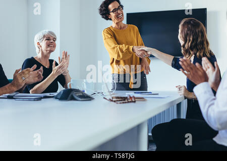 Geschäftsfrauen schütteln die Hände und während eines Geschäftstreffens. Weibliche Profis schütteln sich die Hände, während das Team nach einer erfolgreichen M die Hände klatscht Stockfoto
