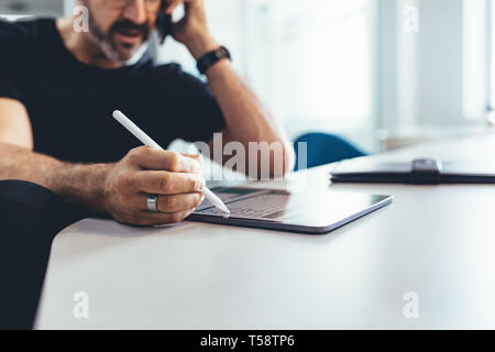 Reifer Mann mit Handy und der Arbeit an seinem digitalen Tablet. Unternehmer arbeiten im Büro, Fokus auf digitale Tablet- und Stifteigenschaften. Stockfoto