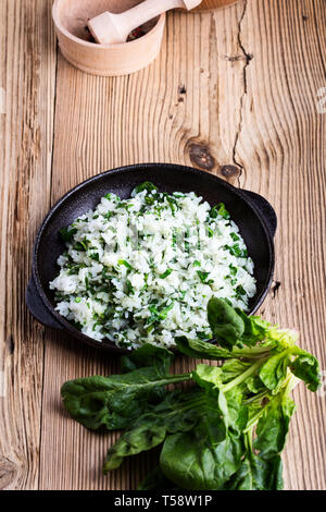 Weißer Reis mit Spinat in Gusseisen Skillet auf rustikalen Holztisch serviert mit frischen grünen Blattgemüse, auf pflanzlicher Basis Mahlzeit, Nahaufnahme, selektive foc Stockfoto