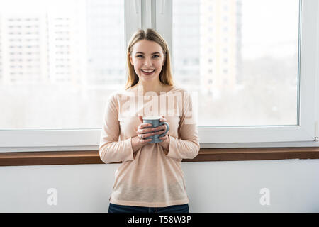 Jung und hübsch Dame saß auf dem Fensterbrett und Blick aus dem Fenster mit der Tasse Kaffee am Morgen Stockfoto