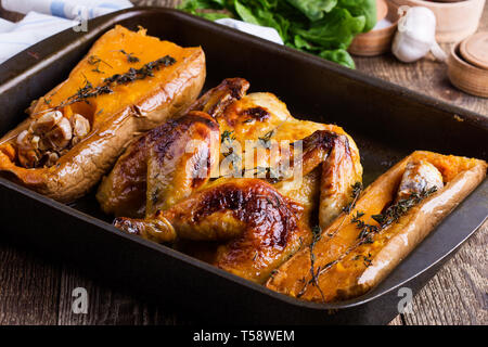 Gebratenes Huhn mit saisonalen Herbst Kürbis, Knoblauch und Kräuter in der Backform auf Holz rustikal Tisch, Nahaufnahme, selektiver Fokus Stockfoto