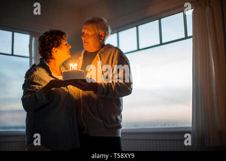 Gerne älteres Paar feiert Geburtstag mit einem Geburtstagskuchen. Stockfoto