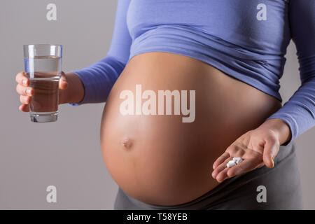 Bild der schwangeren Frau, die Einnahme von Tabletten und ein Glas Wasser auf grauem Hintergrund. Stockfoto