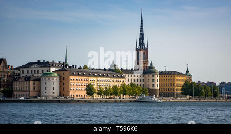 Das westliche Ufer des Riddar Holmen (des Ritters Islet) mit dem Turm und die Turmspitze der Kirche Riddarholm und seinen bunten historischen Gebäuden. Stockfoto