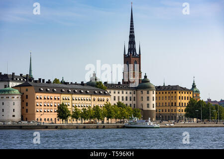 Das westliche Ufer des Riddar Holmen (des Ritters Islet) mit dem Turm und die Turmspitze der Kirche Riddarholm und seinen bunten historischen Gebäuden. Stockfoto