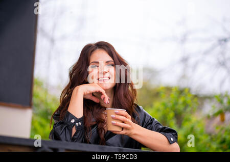 Smilie junges Mädchen in Smart Casual eklektische Outfit sitzt auf der Terrasse des Cafés bei Kaffee Trinken aus dem Kelch. Coffee to go Stockfoto