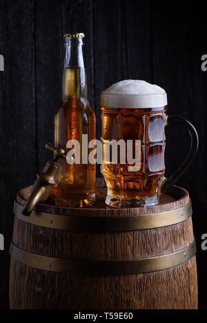 Bier Glas und Flasche auf vintage Holzfass mit alten, dunklen Hintergrund Stockfoto