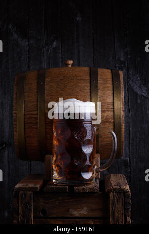 Riesige Bierkrug auf alten Holzkiste mit Vintage Barrel Bier auf Hintergrund Stockfoto