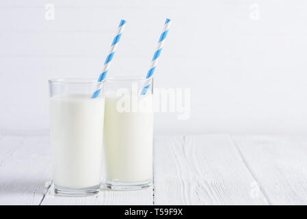 Zwei Gläser Milch mit blauen abgestreift Papier Stroh auf weiße Holztisch still life Stockfoto