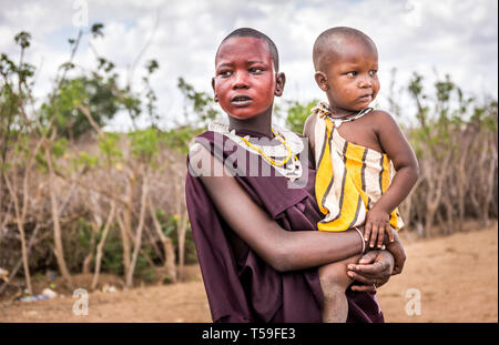 MASAI DORF, KENIA - Oktober 11, 2018: Unindentified afrikanische Frau mit einem Kind, die traditionelle Kleidung in Masai Stamm, Kenia Stockfoto