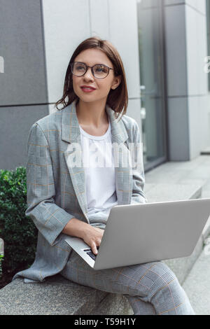 Abstand arbeiten. Junge Dame in Brillen sitzen auf der Straße mit Laptop beiseite, freudige Stockfoto