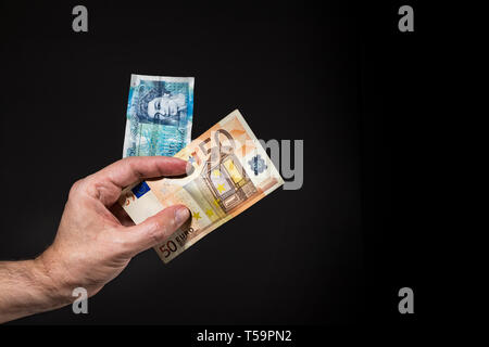 Eine männliche Hand mit einem fünf Pfund und 50 (fünfzig) Euro Banknoten, brexit Konzept, über Schwarz isoliert. Stockfoto