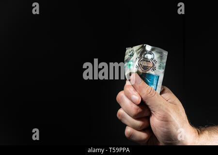 Eine männliche Hand mit einem fünf Pfund Banknote auf seine Faust, über Schwarz isoliert. Stockfoto