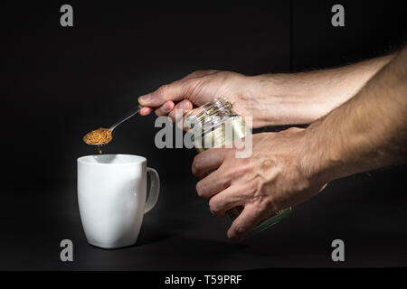 Männliche Hand gießen granulierten Instant Kaffee auf einer weißen Tasse, über Schwarz isoliert. Stockfoto