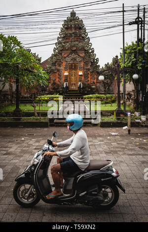 Mann Reiten auf einem Roller vor einem Tempel auf Bali, Indonesien Stockfoto