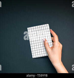 Blick von oben auf die Frau Hände mit Stilvolle Maniküre holding Notizblock mit Kopie Speicherplatz auf schwarze Farbe Papier Hintergrund im minimalistischen Stil. Vorlage für feminine Stockfoto