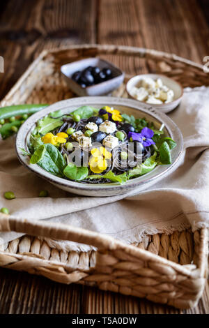 Vegetarische schwarze Bohne Nudelsalat mit Blattgrün, Oliven, grüne Erbsen, Schafskäse, mit essbaren Blüten dekoriert Stockfoto