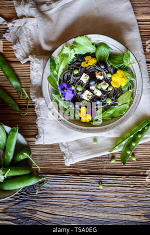 Vegetarische schwarze Bohne Nudelsalat mit Blattgrün, Oliven, grüne Erbsen, Schafskäse, mit essbaren Blüten dekoriert Stockfoto