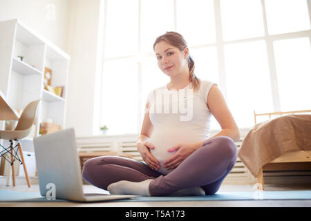 Schwangere Frau sitzt auf der Yogamatte Stockfoto