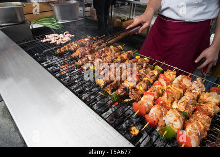 Food-Konzept. Gut aussehend Jungkoch in weißen Uniform überwacht den Grad der Röstung und dreht sich Fleisch mit der Zange im Inneren der Restaurantküche. Stockfoto