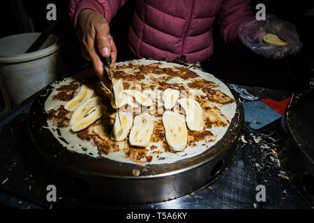 Kochen Pfannkuchen mit Banane und Schokolade einfügen. Straße süße Speisen bei Nacht Markt in Asien. Stockfoto