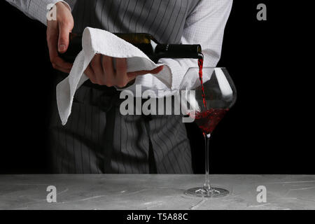 Rotwein in Glas gießen. Barkeeper auf Kellner Konzept auf schwarzem Hintergrund. Stockfoto