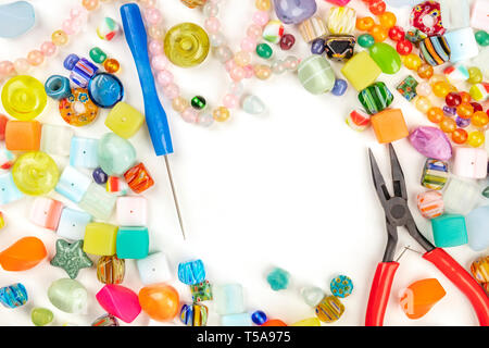 Ein Foto von vielen unterschiedlichen Perlen mit Werkzeugen für die Herstellung von Schmuck, auf weißem Hintergrund mit Kopie Raum Stockfoto