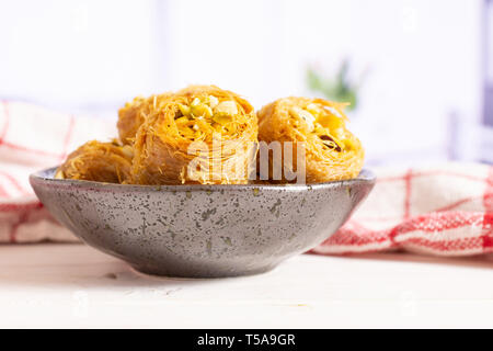 Menge ganz süße Libanesen baklava Stück Vogelnest Vielfalt auf grau Keramikplatte mit einem Küchenhandtuch in einem weißen Küche Stockfoto