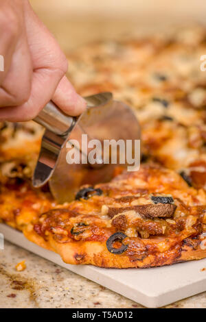 Man schneiden ein Stück hausgemachten Fleisch und vegetarische Pizza mit Belag an Wurst, Salami, Canadian Bacon, schwarze Oliven, Champignons, Mozzarella, Stockfoto