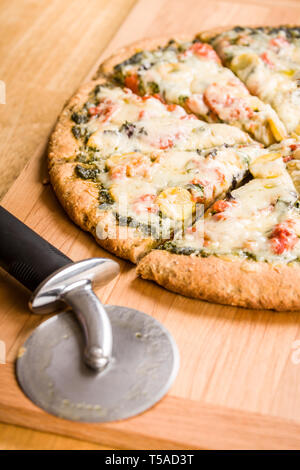 Pizza Cutter und einem frisch gebackenen, Vegetarisch, Pesto, multi-Grain, Pizza mit dicker Kruste Stockfoto