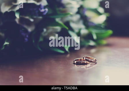 Schöne Hochzeit Ringe liegen auf einem Holz- Oberfläche vor dem Hintergrund der einen Blumenstrauß Stockfoto