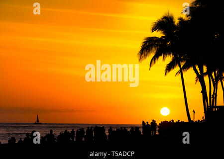 Massen von Touristen sammeln eine orange Sonnenuntergang am Strand von Waikiki Honolulu, Oahu Hawaii USA zu beobachten Stockfoto