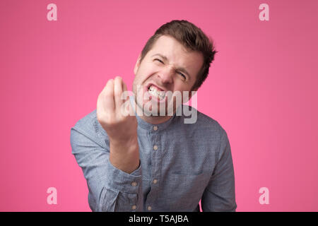 Hübscher junger Mann auf der Suche wütend zeigen italienische Geste über rosa Hintergrund. Stockfoto