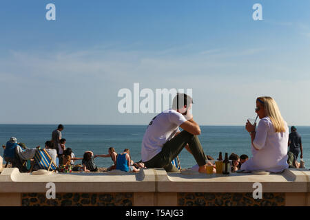 Paar an der Wand vor dem Strand sitzt. Brighton, East Sussex, Großbritannien Stockfoto